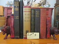 Front view of the lot with six vintage books lined up between two wooden carved animal bookends with detailed heads and legs.