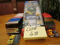 Overview of the lot showing the Buddy L Greyhound bus, packaging of Hot Wheels Dirt Track Race cars, and other loose toy cars on a wooden table.