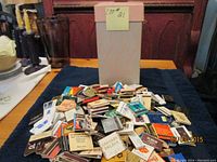 Full view of vintage Eatons cardboard box with a large assortment of vintage matchbooks laid out on table