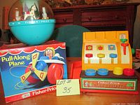 Group photo of the three vintage Fisher Price toys: spinning globe, pull-along plane in box, and cash register toy.
