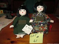Front view of two 9 inch tall Japanese dolls with porcelain-like faces and traditional kimono clothing, tags visible attached to one doll.