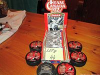 Top view of five hockey pucks arranged around the red box containing unopened packs of Team Canada 20th Anniversary hockey cards.