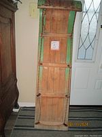 Front view of vintage wooden toboggan showing slatted wooden underside, green painted edges, and leather straps across width.