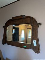 Front view of the antique mirror mounted on the wall showing the bevelled glass and carved wooden frame with scroll details.