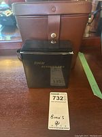 Brown carrying case with black box labeled 'Zoom Binoculars' and auction lot number card on wooden surface.