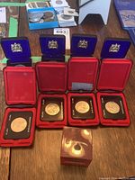 Four Manitoba Centennial 1970 silver dollar coins in black plastic holders and red velvet-lined protective cases with crests on open lids, arranged in a row.