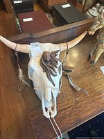 Front view of ceramic cow skull with indigenous woman medallion and hanging feathers.