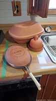 Photo showing large clay baker, clay garlic keeper, and LaCotta clay pan on kitchen counter.