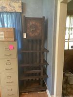 Full view of tall narrow Mission Style wooden clock with multiple shelves beneath the clock face.