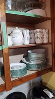 Wooden kitchen shelf holding stacked ivy pattern Corelle dishes including cups, saucers, teapot, creamer, sugar bowl, small plates, and bowls