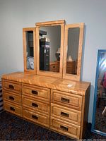 Front view of the wood dresser showing nine drawers with brass recessed handles and the large central mirror framed in wood with two smaller hinged side mirrors