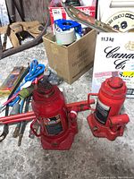 View of two red hydraulic bottle jacks and assorted electrical connectors and cords on a concrete floor.