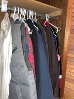 Six assorted jackets and one vest hanging on a closet rod.