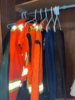 Wide shot of hanging outerwear including hi-vis coats, green slicker, coveralls, vests and jacket
