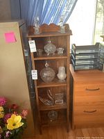 Full view of wooden shelf displaying all pressed glass items with two tall candle holders on top, candy dishes, swan figurine, and footed bowl on shelves.