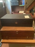 Photo of two storage boxes stacked, one black with latch, one wooden with drawer pulls.