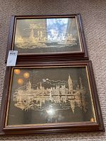 Pair of wood framed prints showing reverse sterling silver cityscape silhouettes with reflections, on black backgrounds. Frames on carpet floor.
