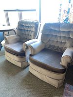 Front angle view of both matching swivel base armchairs showing tufted back, matching color scheme, and skirted base.
