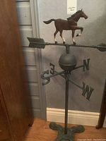 Full side view of the weather vane showing the horse figure on arrow and directional letters on stand.