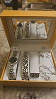 Box set containing watch with black face, bracelet, necklace, and earrings arranged in a presentation case with mirror lid