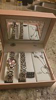 Photo of the four-piece set displayed inside a jewelry box with mirror, showing watch, bracelet, necklace and earrings.