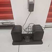 Image showing the full setup of Centrios Duet wireless speakers with the iPod dock station plugged into a wall outlet, illuminated blue power indicators on speakers.