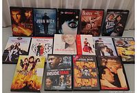 Photo displaying the lot of 14 DVDs and 1 VHS tape arranged in rows on a flat surface for identification.