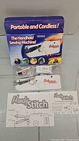 Compact white Handy Stitch handheld sewing machine with accessories and original packaging box with product images and text describing cordless sewing convenience.