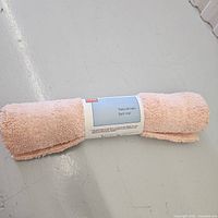 Rolled peach orange bath mat on a white floor, wrapped with label.