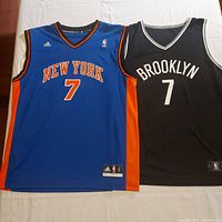 Front view of both jerseys laid flat showing team names, numbers, logos, sizes