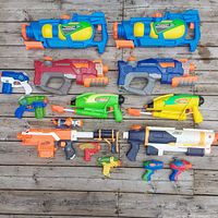All 14 water guns laid out on wooden deck showing variety and condition