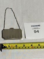 Front view of the silver-tone rectangular compact purse with chain handle on white fabric, showing the size against a measuring tape.