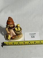 Full front view showing the seated girl with chicks and measuring tape showing approximately 5 inches tall.