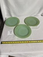 Three jade green Fire-King diner plates arranged on a white cloth with a measuring tape showing about 9.5-10 inches diameter.