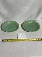 Two light green jadeite glass bowls side by side with a measuring tape in front showing approximate size.