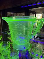 T & S uranium Vaseline Depression glass measuring cup shown under UV light to highlight glowing properties and measurement markings.