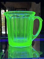 Green uranium glass pitcher glowing under UV light showing vibrant green color and vertical ridges.