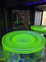 Three vaseline uranium glass plates glowing bright green under UV light, showing the vintage roulette design by Hocking Glass.