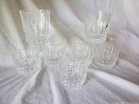 Seven clear crystal whiskey glasses arranged on white fabric to show quantity and condition.