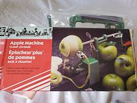 Apple Peeler Machine box showing product image and label in English and French describing it as a clamp-on base apple peeler that peels, cores, and slices apples.