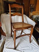 Front and angled view of a single wooden chair with curved back and restored cane seat.