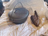 Photo showing Dutch oven with lid and sad iron together on a white sheet, visual condition and material detail