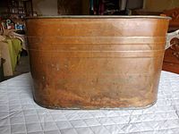 Front view of the oval copper bin showing wear and patina on the surface.