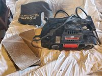 Full view of Craftsman belt sander showing included extra sanding belts and dust collection bag on a light surface.