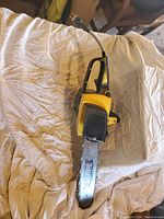 Yellow and black electric chainsaw with 14-inch blade laid flat on white cloth background, power cord visible