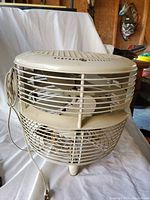 Front and top view of vintage General Electric fan showing cream color, cylindrical design, grills, and logo.