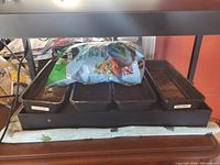 Full view of the grow light unit showing 4 planting trays inside a water reservoir tray with a wet mat. Seedling labels visible on trays.