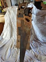 Six used handsaws with wooden handles leaned against a wooden case, exhibiting rust and wear on blades, photographed on a white sheet