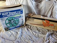 Photo showing boxed hose reel and boxed hedge trimmer side by side on fabric surface