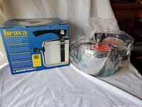 Photo of the boxed Lagostina Brava pressure cooker alongside the cooker itself wrapped in plastic on a white surface.